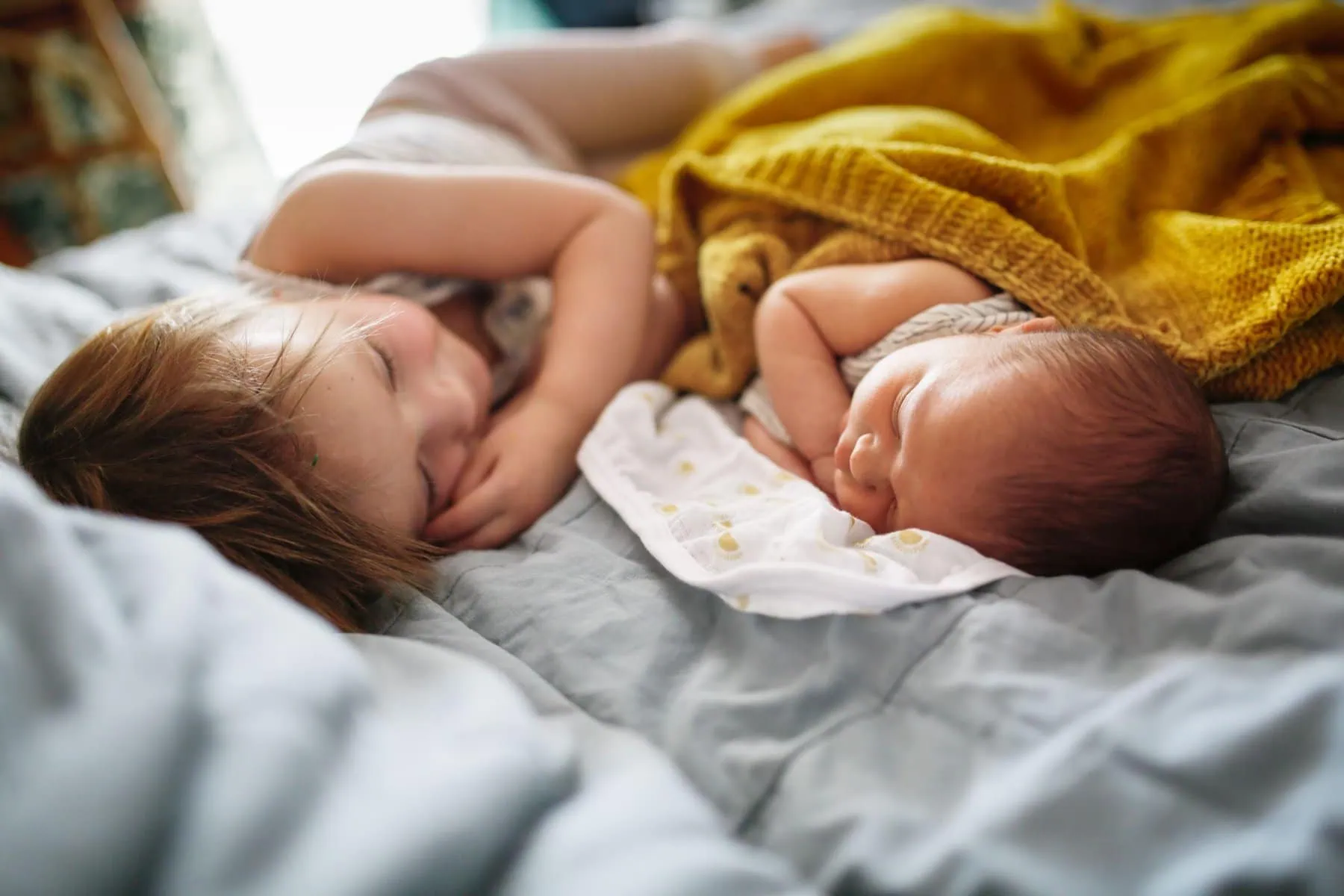 A young girl and a baby lying down on a blanket and looking cosy.