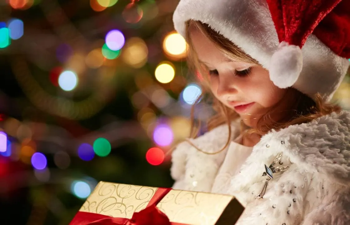 A young girl dressed as Santa holding a present.