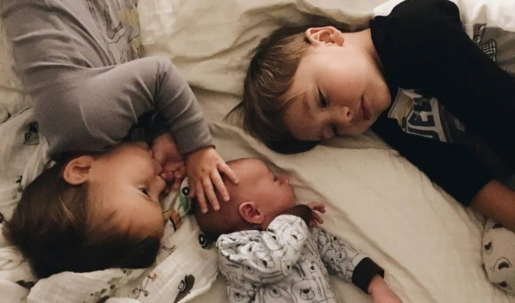 Three young children lying down and looking cosy.