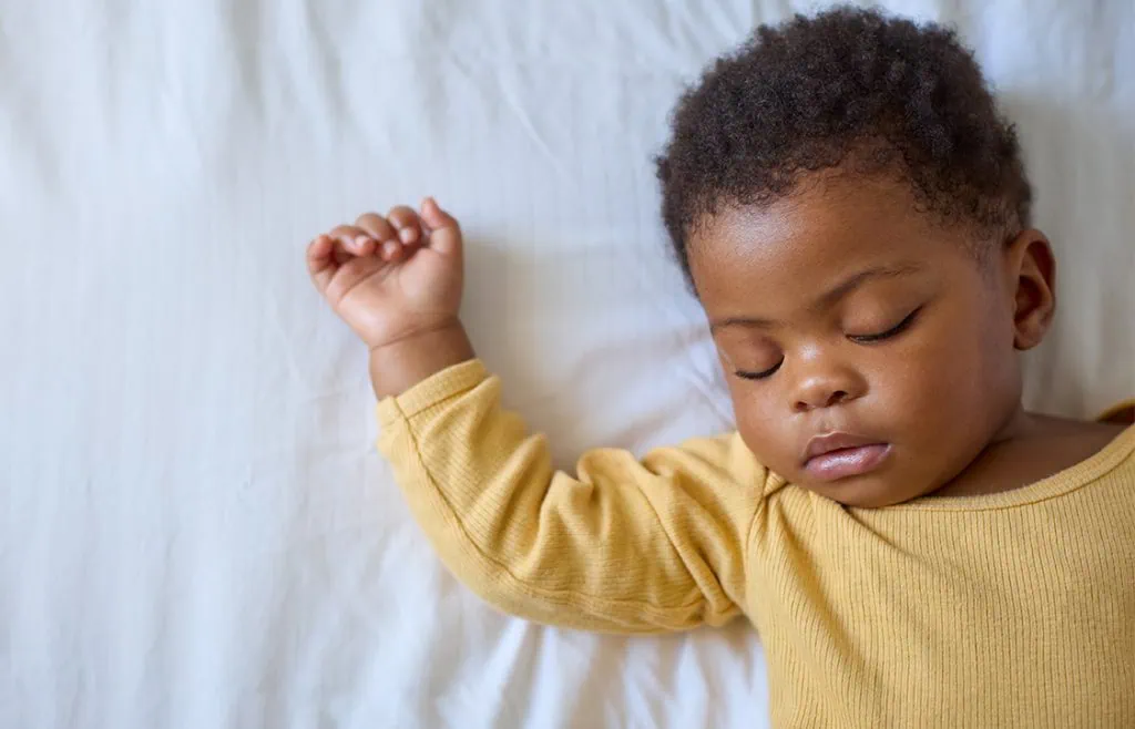 Close-up of a young child peacefully sleeping on a white bed in yellow clothes, showcasing early childhood development.