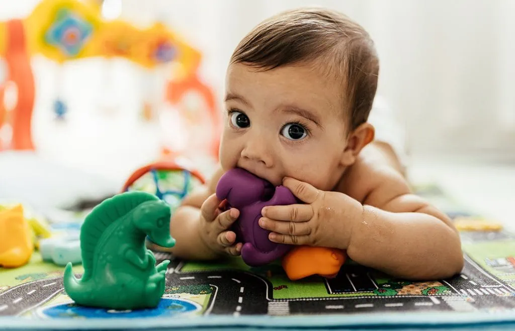 Adorable baby playing with colourful baby toys, lying on playful mat indoors.