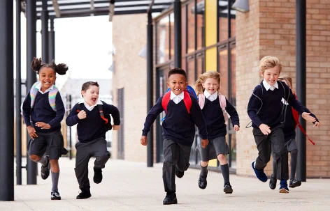 Happy school children running outdoors in uniform.