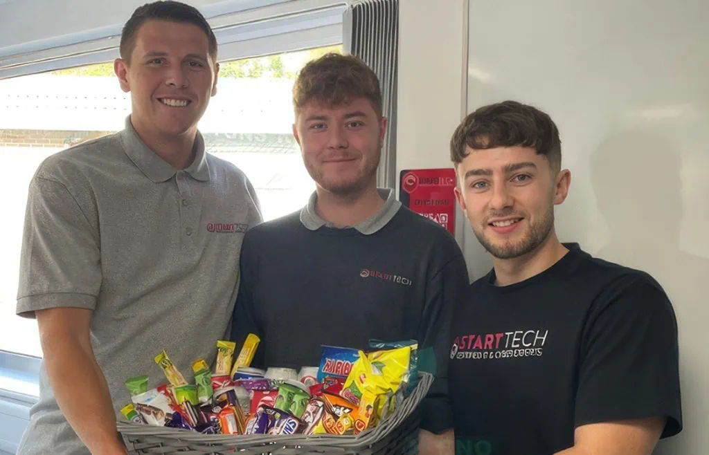 Young men holding a basket of snacks and treats for children.