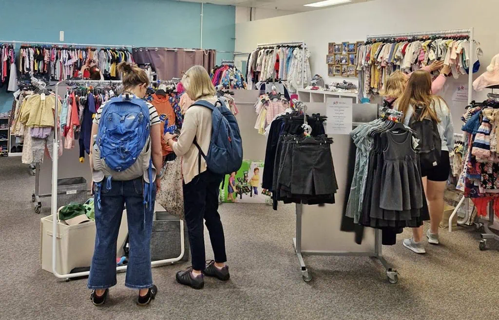 Happy children browsing children’s clothes at Little Stars thrift store in the UK.