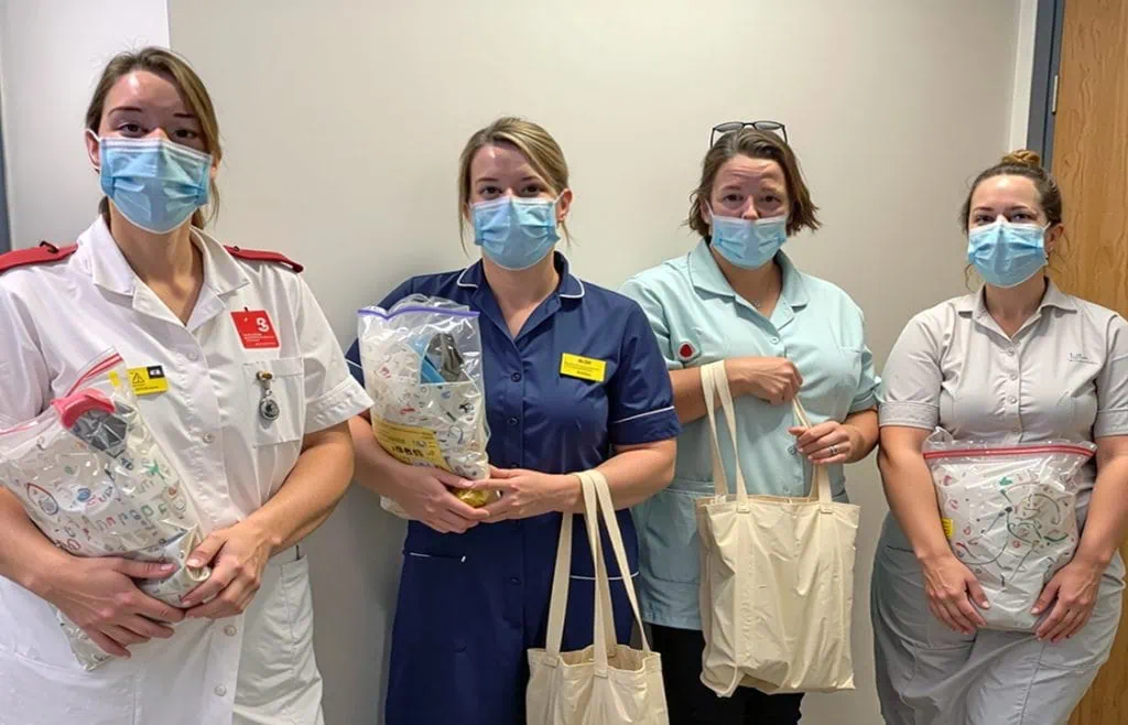 Nurses holding care packages in healthcare setting, wearing masks, representing support and compassion.