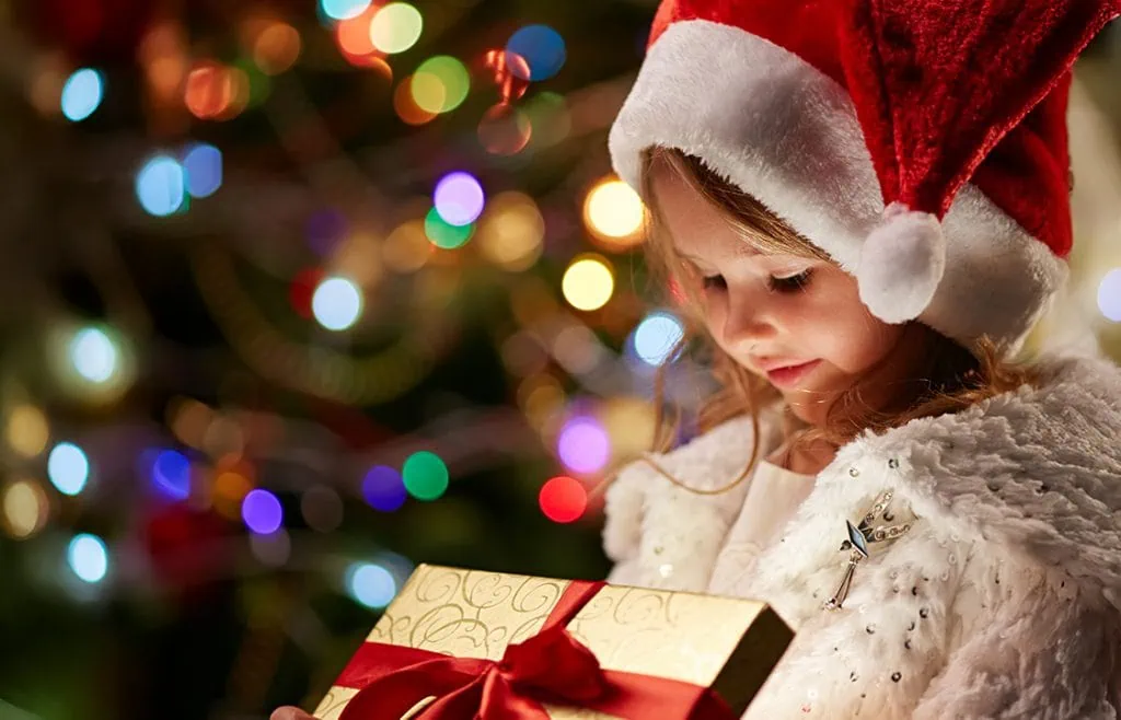 Child in Santa hat holding wrapped Christmas present, festive holiday celebration and gift exchange.
