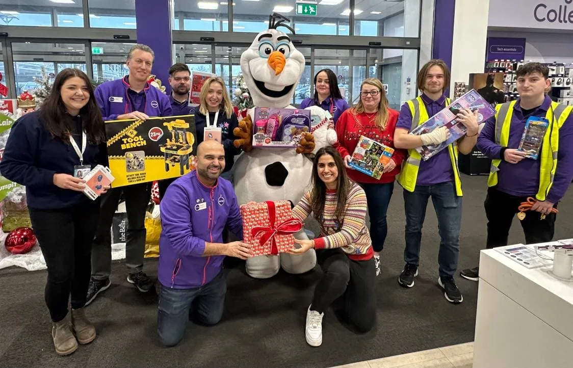 Cheerful group with holiday toys and mascot at Little Stars charity event, spreading joy to children this Christmas.