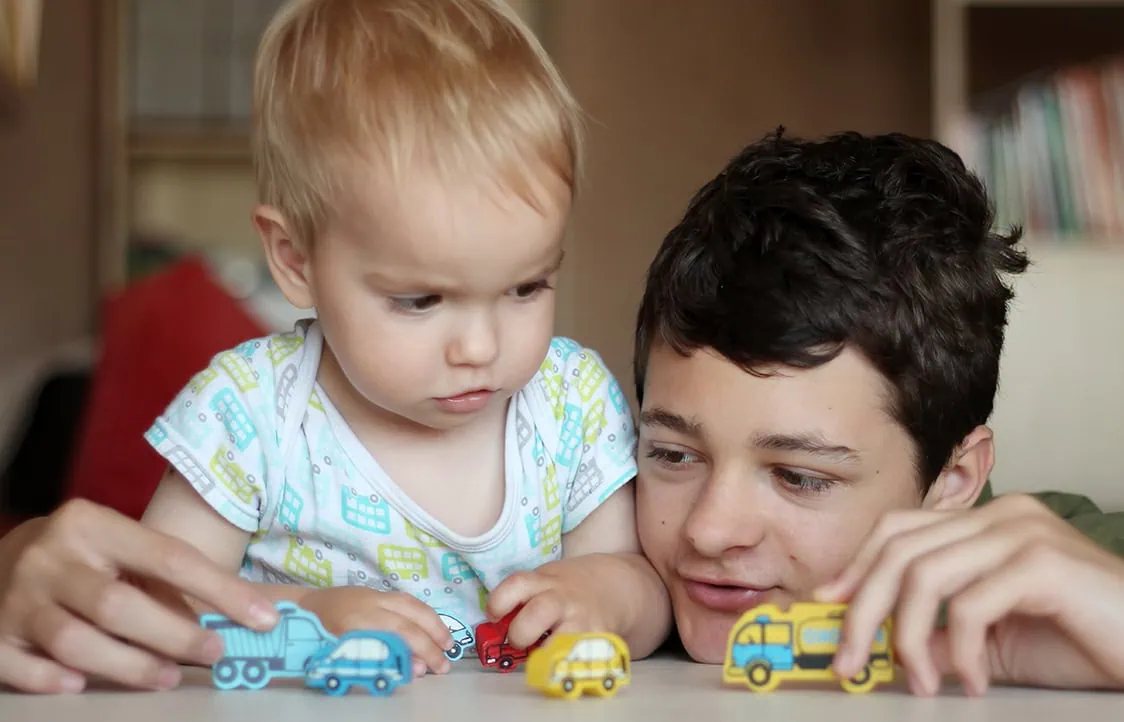Young child and teenage boy playing with toy cars, indoors, focus on children and toys.