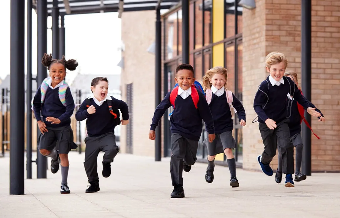 Happy children in school uniforms running outside.
